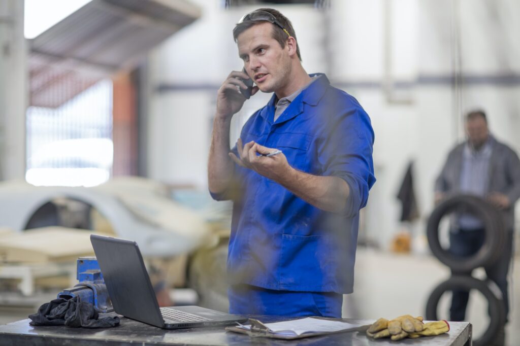 Car mechanic making smartphone call in repair garage